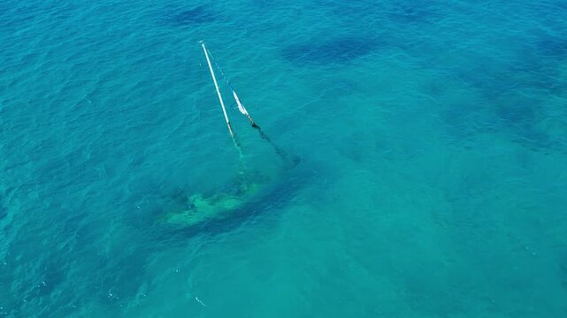 Aerial shot stranded sailboat near reef, shallow turquoise sea exposing mast and shadowed hull, calm swell with sun glint, drone circumnavigating target for inspection, mapping, Maldives