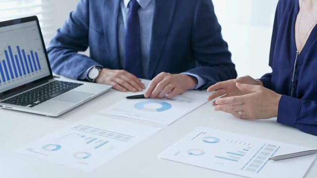 Business partners are discussing company performance and making plans based on charts and graphs displayed on laptop and printed documents. Business people and finance concept
