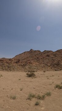 Panning shot of a dry, rugged desert mountain landscape with sparse shrubs.