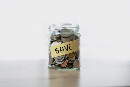 Glass jar filled with coins with a label that says SAVE on a wooden table. Representing concepts such as money saving, financial planning, investment and budget management.