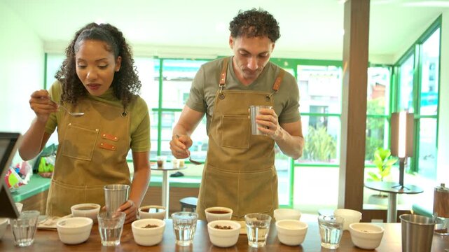 Two coffee professionals tasting multiple coffee samples with spoons during a sensory evaluation session in a specialty coffee shop