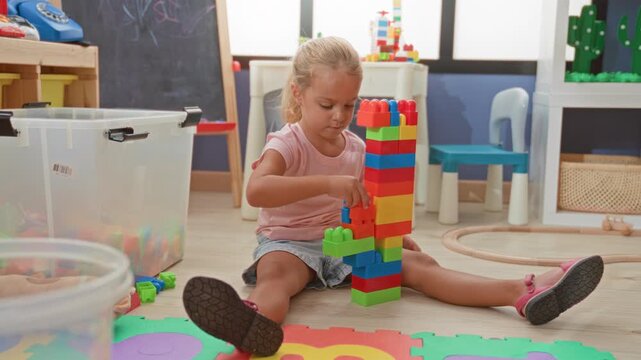 Little girl stacking colorful plastic blocks into a tall tower in a playroom; concentration creativity.