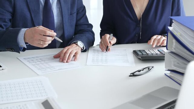Business colleagues are reviewing financial reports and using a calculator during a productive meeting in a brightly lit office setting. Audit and taxes in business