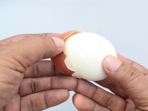 Close up of hands peeling the shell of a freshly boiled brown chicken egg, revealing a smooth white egg white, ready to eat for breakfast or a healthy meal