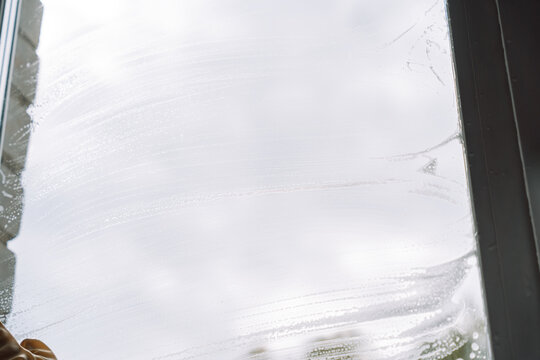 Broad cleaning streaks on a window with a cropped glove at the lower left.