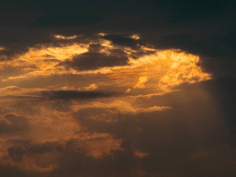 Dramatic orange golden sunset sky with dark storm clouds and glowing light breaking through, moody stormy cloudscape at dusk, atmospheric background