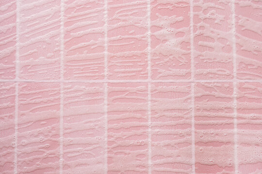 Fine curved cleaning foam streaks across pink tiles in overhead view.