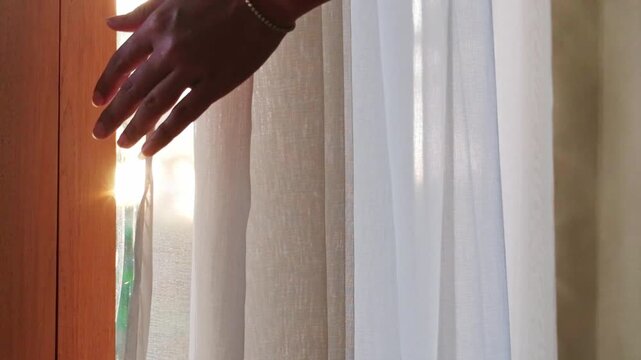 woman's hand She opened the curtains on the window. There was morning light through the window in her room, looking at the view of the mountains and trees as the sun rose	
