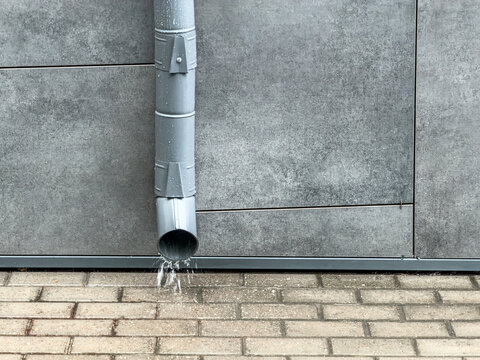 rain water flowing from downspout onto a concrete pavement surface.