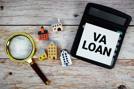 VA Loan text with house model, calculator and magnifying glass on wooden background