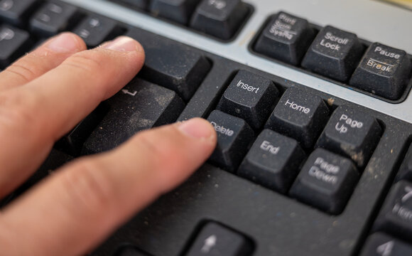 Close-up of a finger pressing the Delete key on a dusty computer keyboard in a woodworking workshop, illustrating deletion, data removal, editing, technology and workplace concepts.