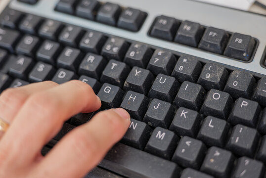 Close-up of a hand typing on a dusty computer keyboard in a woodworking workshop, combining technology, manual work, digital communication, workplace hygiene and industrial production.