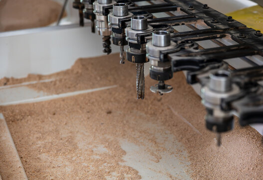 Close-up of CNC router tool holders and milling cutters above a sawdust-covered worktable, showing automated woodworking, precision machining, furniture production and industrial technology.