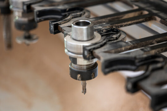 Close-up of CNC router tool holders and milling cutters above a sawdust-covered worktable, showing automated woodworking, precision machining, furniture production and industrial technology.