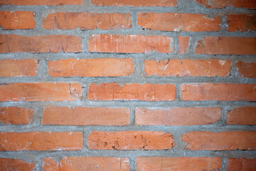 Fototapeta premium Close-up of an exposed red clay brick wall with rough gray mortar joints, creating a rustic masonry texture and architectural background for construction and renovation concepts. 