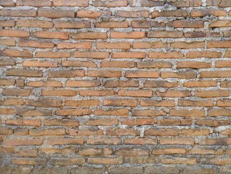 Old weathered red brick wall texture with rough concrete mortar background, ideal for architectural design patterns.