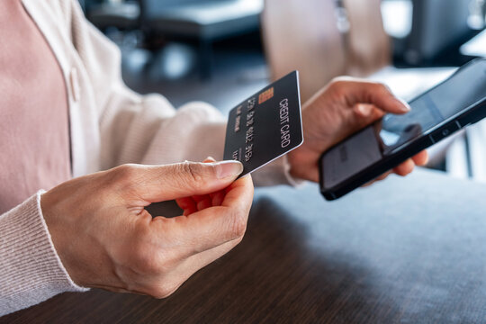 An image of a woman's hand holding a credit card and typing on a smartphone to make a mobile payment, representing concepts of e-commerce, online shopping, and cashless transactions.