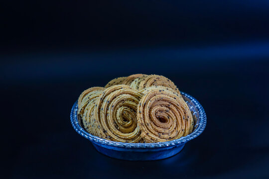High angle view of golden spiral chakli coils arranged in embossed silver plate.