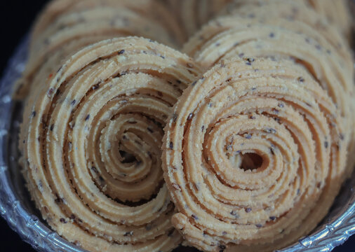Macro detail of spiral chakli murukku coils with sesame seeds on platter.