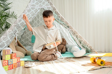 Childhood development and creative play, young boy playing with craft materials inside a cozy indoor teepee tent in a bright nursery room © Pixel-Shot