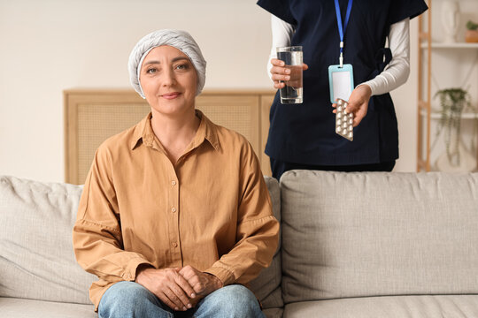 Cancer treatment and home care, patient with headscarf receiving medication from a nurse in a living room setting for oncology support and recovery