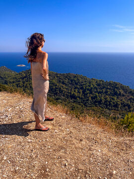 A brunette woman stands in solitude at a scenic viewpoint on Mljet Island, admiring the vast Mediterranean Sea as the gentle breeze moves through her long hair. 