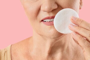 Skincare and healthy aging, senior woman removing makeup with cotton pad for facial cleansing routine and dermatology wellness on a pink background © Pixel-Shot