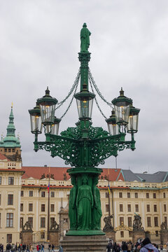 The historic ornate green cast-iron gas street lamp with caryatids and lanterns on Hradčany Square outside the Prague Castle complex.