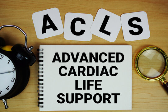 ACLS Advanced Cardiac Life Support text written on notepad with magnifying glass and alarm clock on wooden background