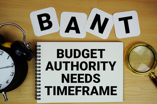 BANT Budget Authority Needs Timeframe text written on notepad with magnifying glass and alarm clock on wooden background
