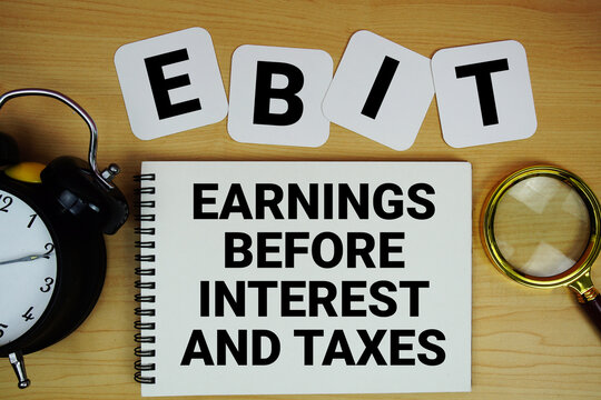 EBIT Earnings Before Interest and Taxes text written on notepad with magnifying glass and alarm clock on wooden background