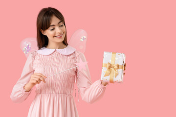 Obraz premium Young woman in fairy costume with wand and gift box on pink background