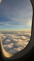 Obraz premium Beautiful scenic view of fluffy white clouds and blue sky at sunset through an airplane window frame during a commercial flight, travel wanderlust and dream destination concept