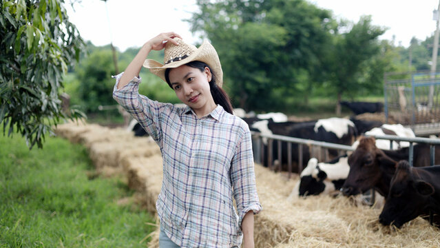 Portrait of Asian female farmer wearing straw cowboy hat standing in front of cow pen on rural livestock farm.