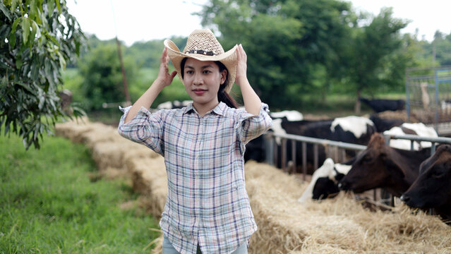 Portrait of Asian female farmer wearing straw cowboy hat standing in front of cow pen on rural livestock farm.