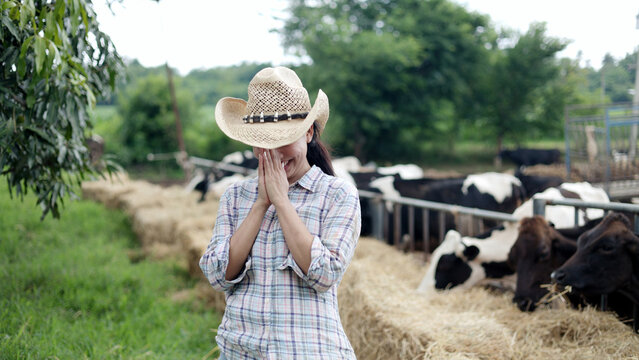 Asian female farmer in straw hat doing Thai greeting wai gesture with hands together at local livestock dairy cow farm.