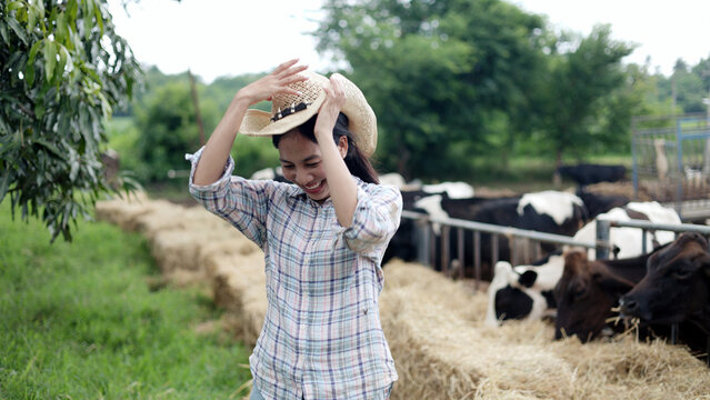 Portrait of Asian female farmer wearing straw cowboy hat standing in front of cow pen on rural livestock farm.