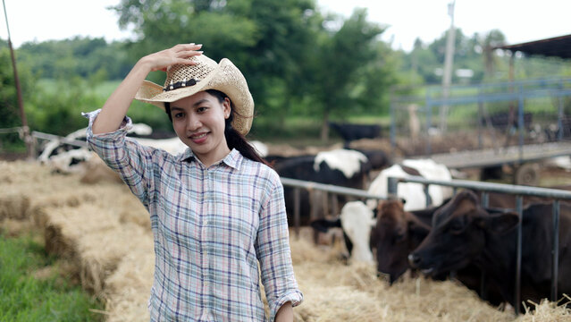 Portrait of Asian female farmer wearing straw cowboy hat standing in front of cow pen on rural livestock farm.