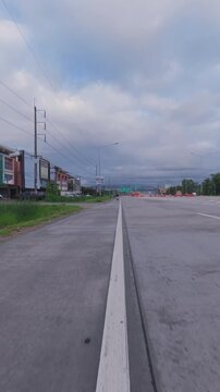 Wide urban roadway under a cloudy sky, with roadside commercial buildings, utility poles and light traffic creating a suburban transportation scene.