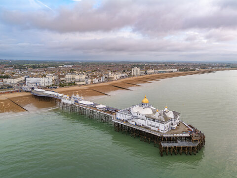High-angle aerial view of Eastbourne Pier and golden dome extending into the English Channel toward the shingle beach and Victorian seafront in East Sussex, England