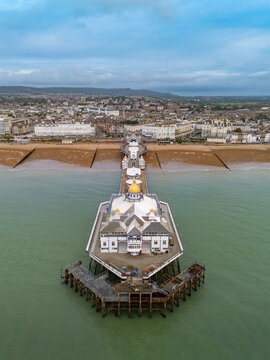 Elevated aerial view looking down the length of Eastbourne Pier toward the town seafront, shingle beach, and Victorian promenade in East Sussex, England