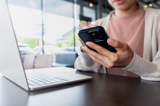 Woman using a smartphone while working and typing. Representing digital lifestyle, mobile communication, technology and modern productivity.
