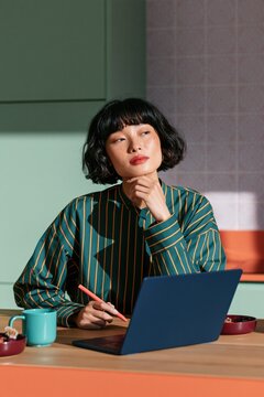Young woman working at laptop in colorful home office with striped shirt for workspace background and creative remote work banner