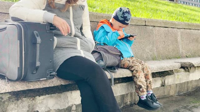 A young boy interacts eagerly with a smartphone. He feels happy and focused while resting on a granite embankment in Saint Petersburg.