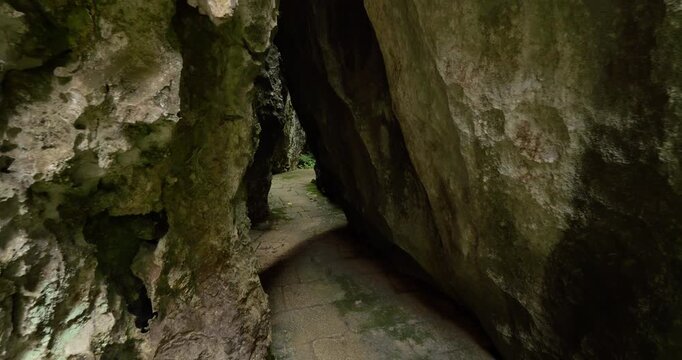 POV walking shot traversing narrow paved stone pathway winding through towering karst limestone walls in Shilin Stone Forest. Atmospheric canyon passage features heavily textured rock surfaces