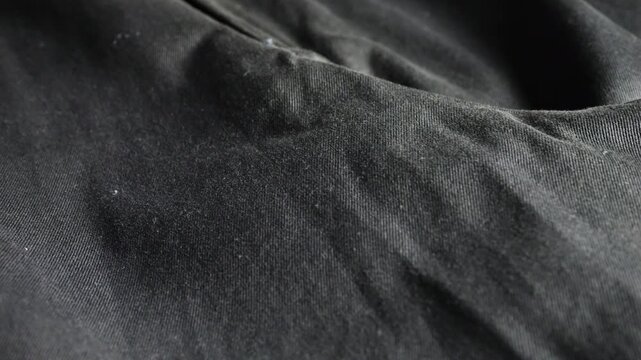 A close-up of black cotton trousers highlights the fabric texture, detailed zipper fly, wide-leg pants, loose-fit slacks, palazzo style, dark woven material, and casual garment structure.