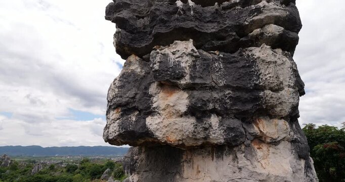Panoramic left pan shot begins with close view of rugged weathered karst textures on nearby towering rock, then revealing sprawling landscape of limestone pillars in lush greenery