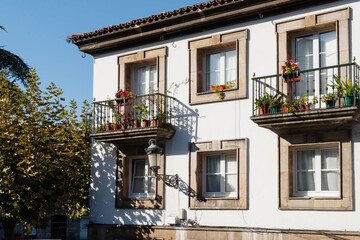 Whitewashed facade with stone framed windows and wrought iron balconies full of potted geraniums in Aviles, Spain. Sunlit old town housing for travel and property rental themes. © Renata