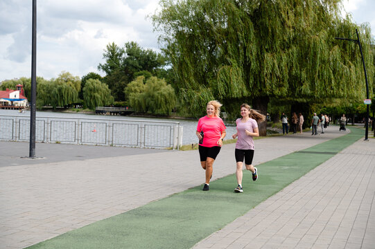 Women jogging together along a path by a river in a park