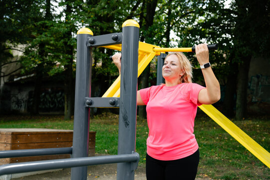 Woman exercises on outdoor pull-up bar in a park during daylight